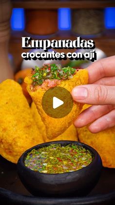 a person holding up a piece of food in front of a bowl filled with salsa