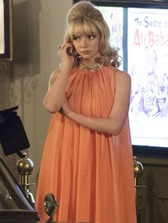 a woman in an orange dress talking on a cell phone while standing next to a piano