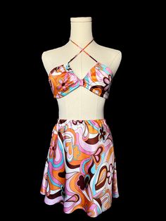 a mannequin wearing a colorful dress on a black background with an orange, pink, and blue design