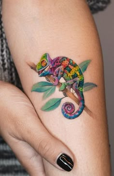 a colorful chamelon tattoo on the left arm and right hand, with leaves around it