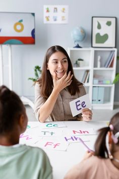 a woman sitting at a table with two children holding up letters to spell out the word