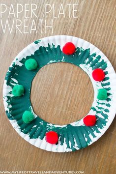 paper plate wreath with pom - poms on it sitting on a wooden table