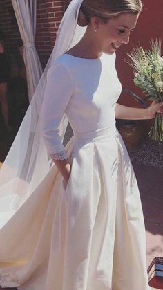 a woman in a white dress and veil walking down the street with a flower bouquet