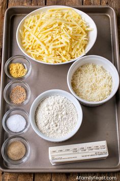 ingredients to make cheese pizza laid out in bowls on a baking tray, including grated cheese and parmesan cheese