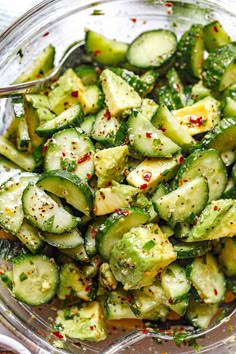 a glass bowl filled with cucumbers and seasoning on top of a table