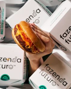 a hand holding a cheeseburger in front of several boxes of pizza sauces