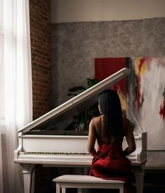 a woman in a red dress sitting at a white piano with her back to the camera