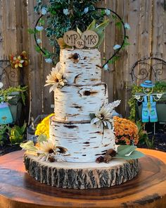 a wedding cake is decorated with flowers and leaves on a wooden table in front of a fence