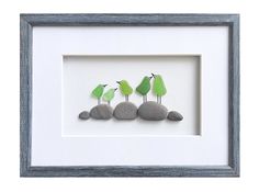 three green birds sitting on top of rocks in a shadow box with a white frame