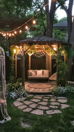 an outdoor gazebo with lights strung over it and a couch in the middle, surrounded by greenery