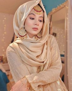 a woman in a white dress with gold jewelry on her head and scarf around her neck