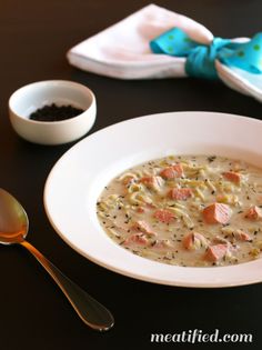 a white bowl filled with soup next to two spoons on top of a table