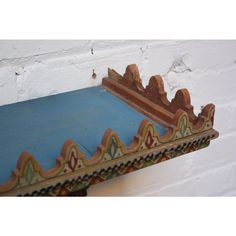 an ornately painted wooden shelf against a white brick wall