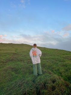 a man standing on top of a lush green field under a blue sky with clouds