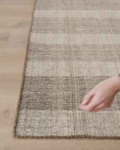 a person is touching the rug on the floor with their hand and pointing at it