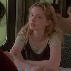 a woman sitting at a table in front of a window with another person looking on