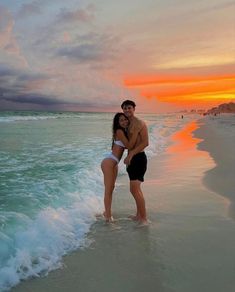 a man and woman standing in the water at sunset on an ocean beach with waves