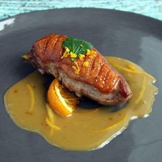 a piece of meat and oranges on a plate with sauce drizzled over it