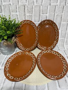 four brown plates sitting on top of a table next to a potted green plant