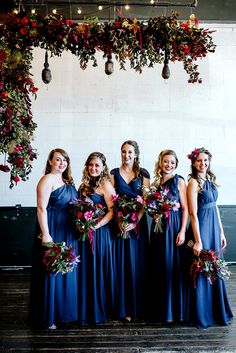 a group of women standing next to each other under a floral covered arch with lights