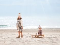 two young children on a beach pulling a sleigh with one child in it