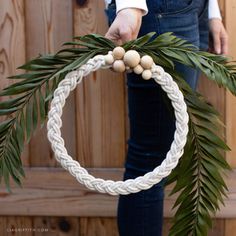 a person holding a wreath made out of rope and wood beads with leaves around it