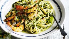 pasta with shrimp and pesto sauce in a white bowl on a table next to a glass of wine