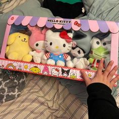 hello kitty stuffed animals in a box on a bed with someone's hand reaching for it