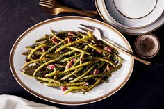 a white plate topped with green beans covered in sauce and seasoning next to silverware