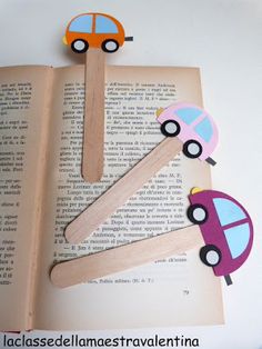 an open book with popsicle cars on top of it and a wooden stick sticking out of the pages