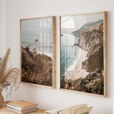 two framed pictures hanging on the wall next to a table with a vase and book