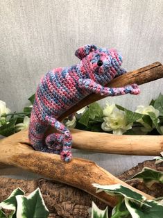 a crocheted teddy bear sitting on top of a wooden branch next to flowers