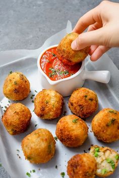 a person dipping some food into a small white bowl with sauce on the side and other appetizers around it