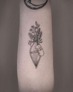 a woman's arm with a tattoo on it and flowers in a vase behind her