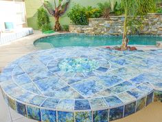 an outdoor pool with blue and green tiles on it's sides, next to a palm tree