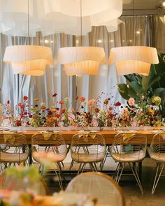 a long table with many chairs and flowers on it in front of some hanging lights