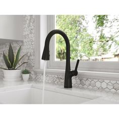 a kitchen sink with black faucet next to a window and potted cacti