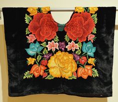 an embroidered piece of cloth with flowers on it hanging from a clothes line in front of a wall