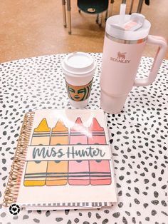 a coffee cup and notebook sitting on top of a table next to a starbucks cup