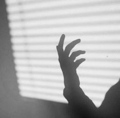 the shadow of a person's hand in front of a window with blinds on it