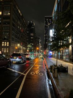 a city street at night with cars parked on the side walk and buildings in the background