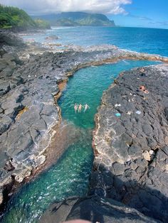 two people are swimming in the ocean near some rocks