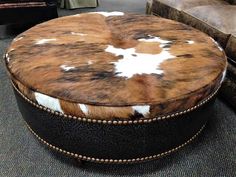 a brown and white cowhide ottoman sitting on top of a carpeted floor