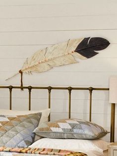 a bed with two pillows and a feather on the wall above it, next to a night stand