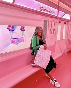 a woman sitting on the side of a pink subway car holding onto a sign that says new york