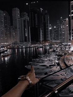 a person points at boats docked in the water next to tall buildings and skyscrapers