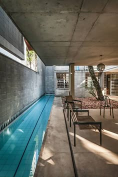 an indoor swimming pool with chairs next to it and a tree in the background,