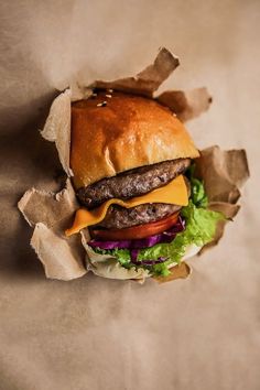 a cheeseburger with lettuce, tomato and onion in a paper wrapper