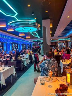 people sitting at tables in a restaurant with blue lights on the ceiling and white tablecloths