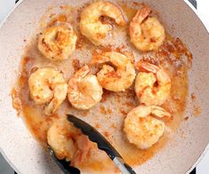 cooked shrimp in sauce being stirred with tongs